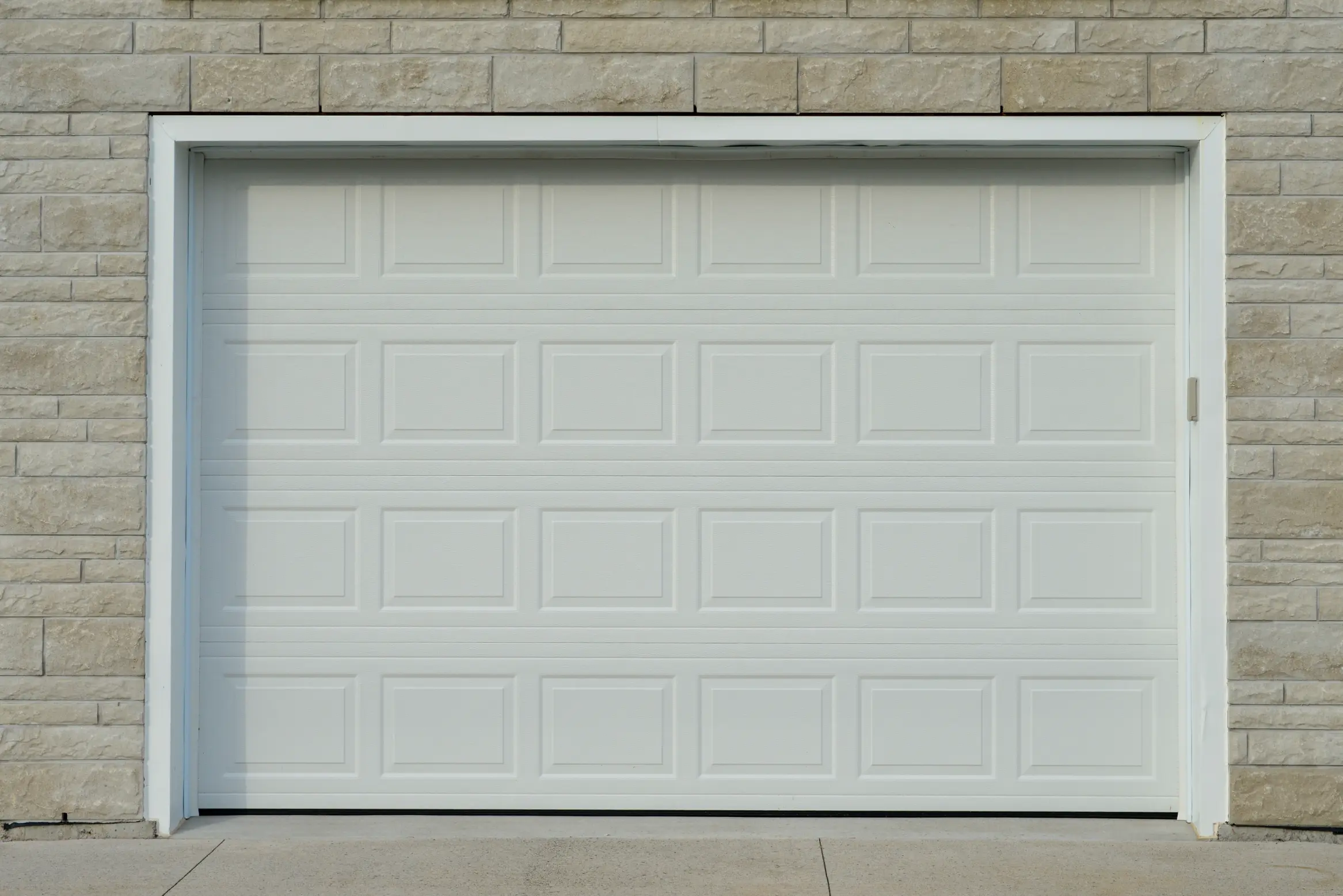 A large white metal car garage door on a grey brick house